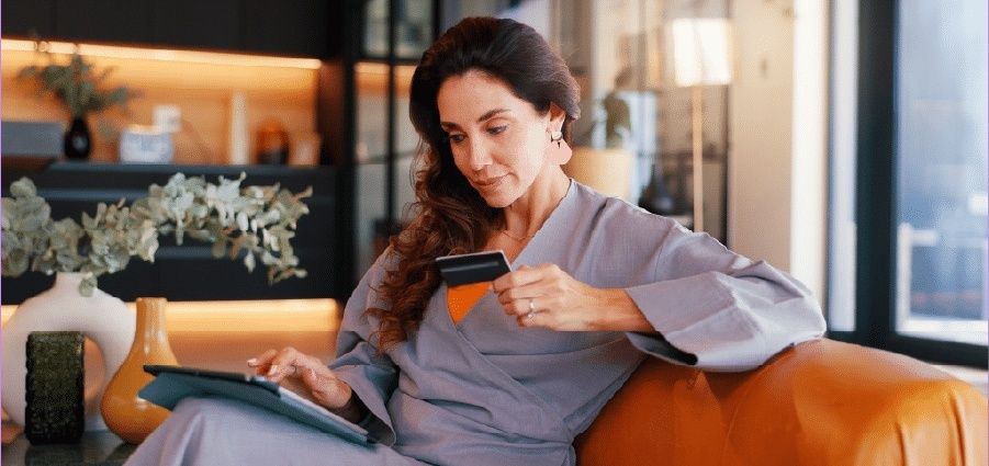 Frau hält eine Zahlungskarte und arbeitet am Tablet im modernen Wohnraum